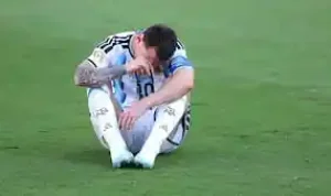 Leonel Messi Lionel Messi duduk di lapangan rumput dengan kepala menunduk sambil memegang wajahnya.