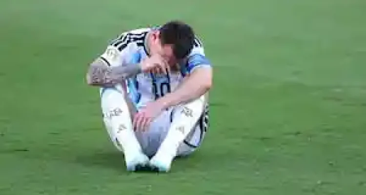 Lionel Messi duduk di lapangan rumput dengan kepala menunduk sambil memegang wajahnya.