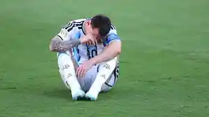 Lionel Messi duduk di lapangan rumput dengan kepala menunduk sambil memegang wajahnya.